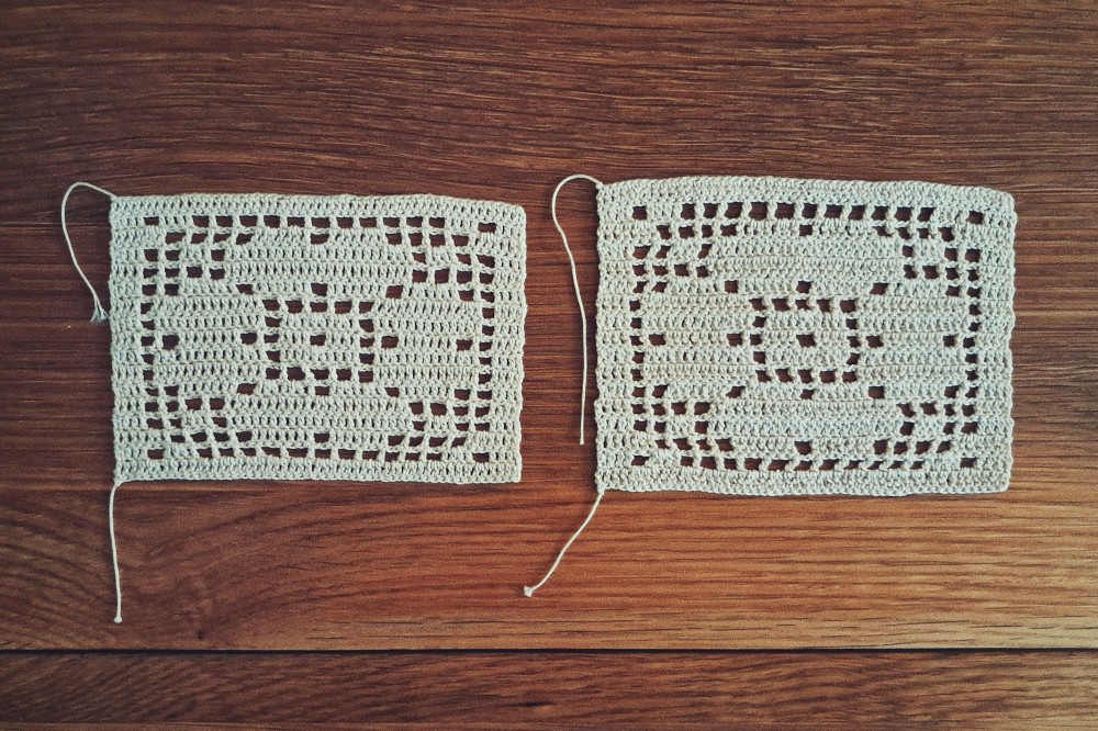A horizontal colour photograph of two filet crochet works of a four petals flower. They are on a wooden table. The design on the left is a little squatter than the one on the right.