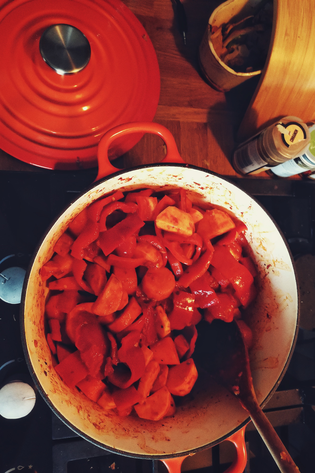 A vertical colour photograph of an selection of orange and red vegetables in a big Le Creuset type casserole dish over a cooker.