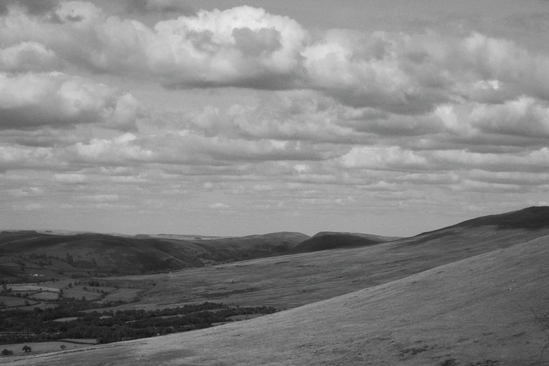 A horizontal black and white photograph of hills and speckled woodlands.