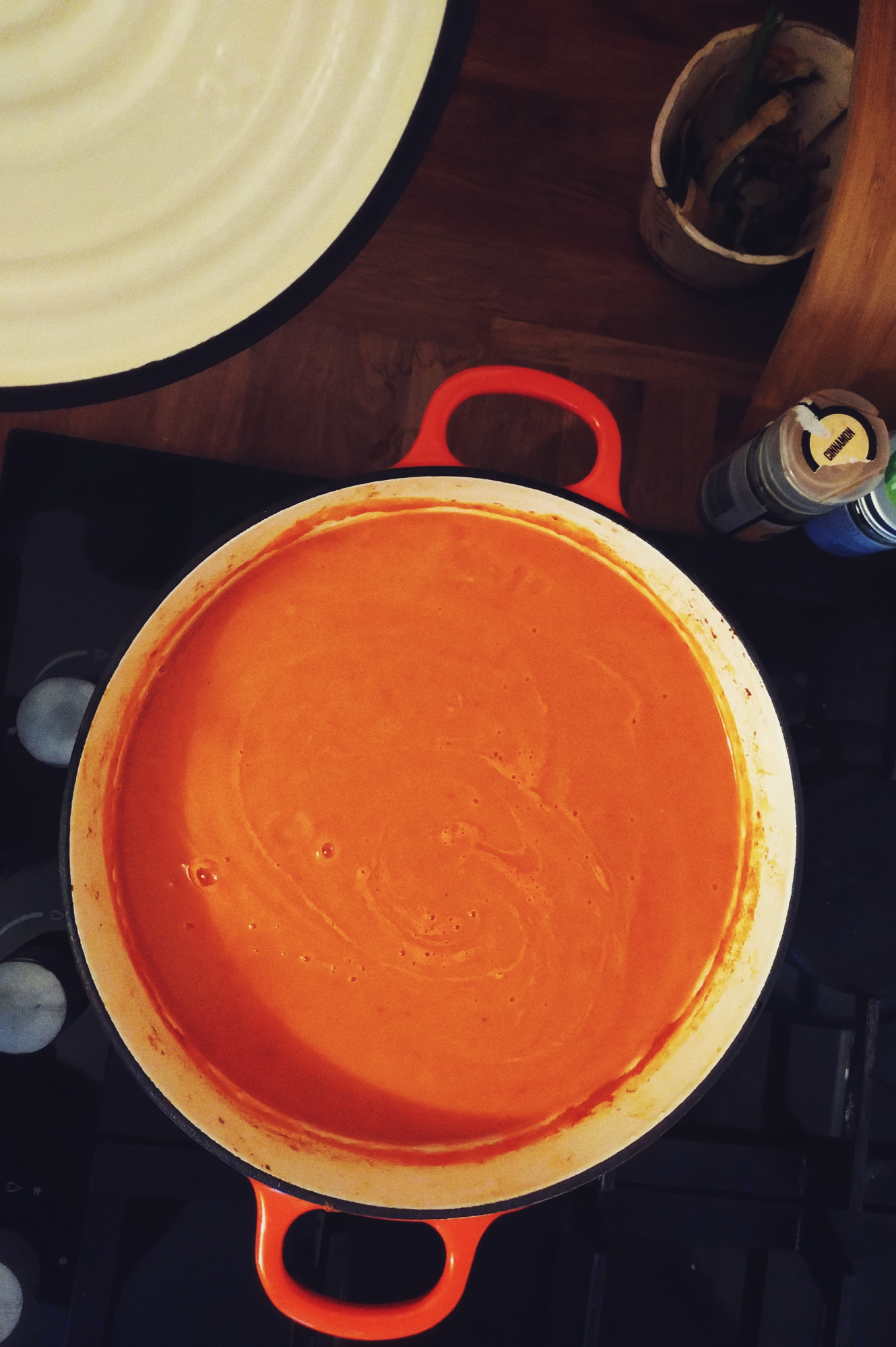 A vertical colour photograph of an orange red soup in a big Le Creuset type casserole dish over a cooker.