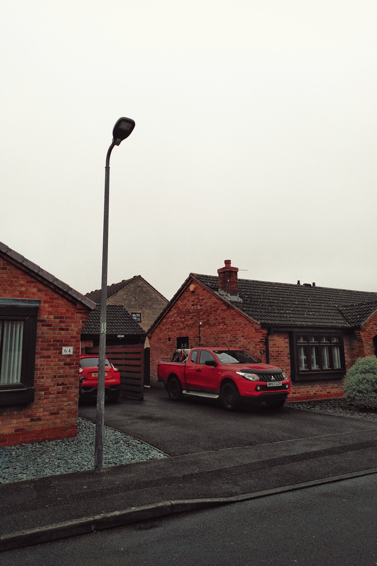 A vertical colour photograph of a handful of brick houses under a milky white sky. But the houses are two red cars.