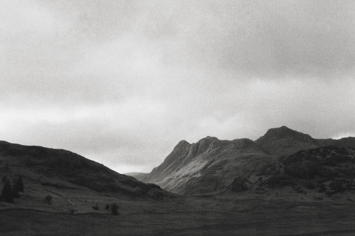 A horizontal black and white photograph of hills in the Lake District in the UK. There is a gap between them filled with light.